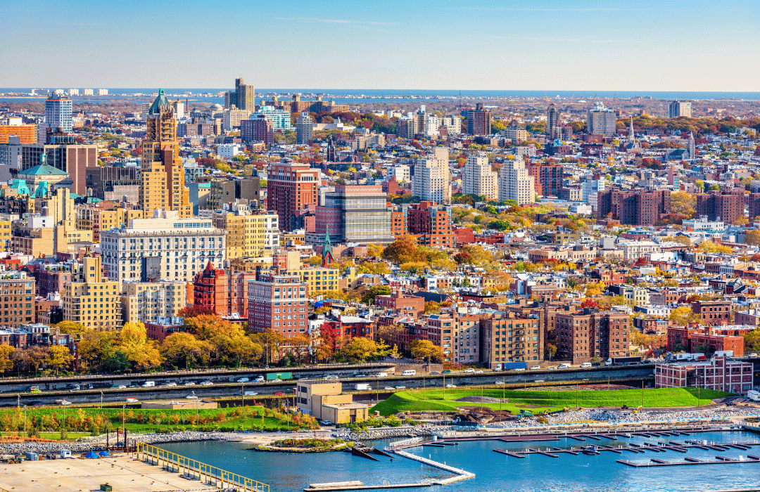 Aerial view of Brooklyn showcasing a mix of residential and commercial buildings, vibrant fall foliage, and waterfront areas, reflecting the neighborhood's diverse architecture and community character.